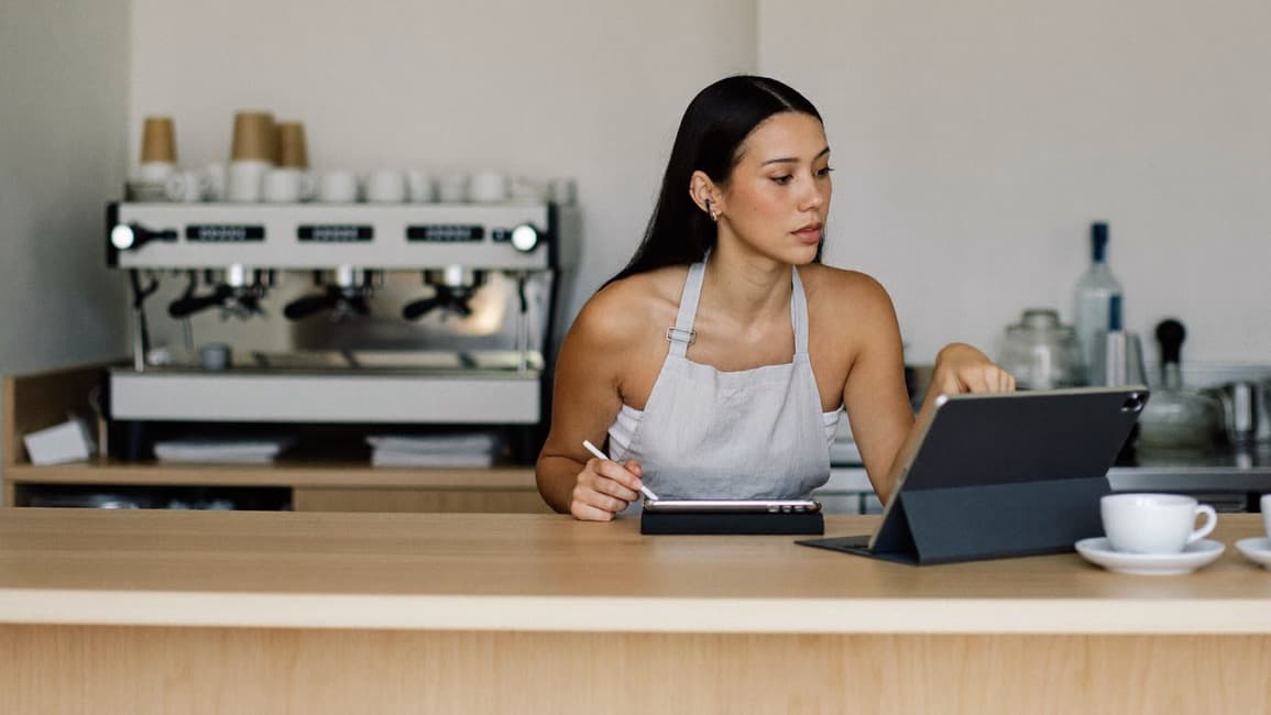 A cafe owner reviewing numbers on a tablet behind her espresso counter