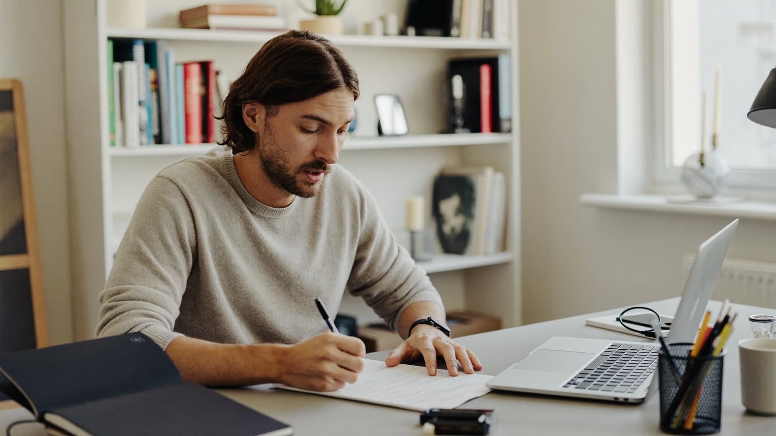 An independent consultant taking notes during a video call in his home office