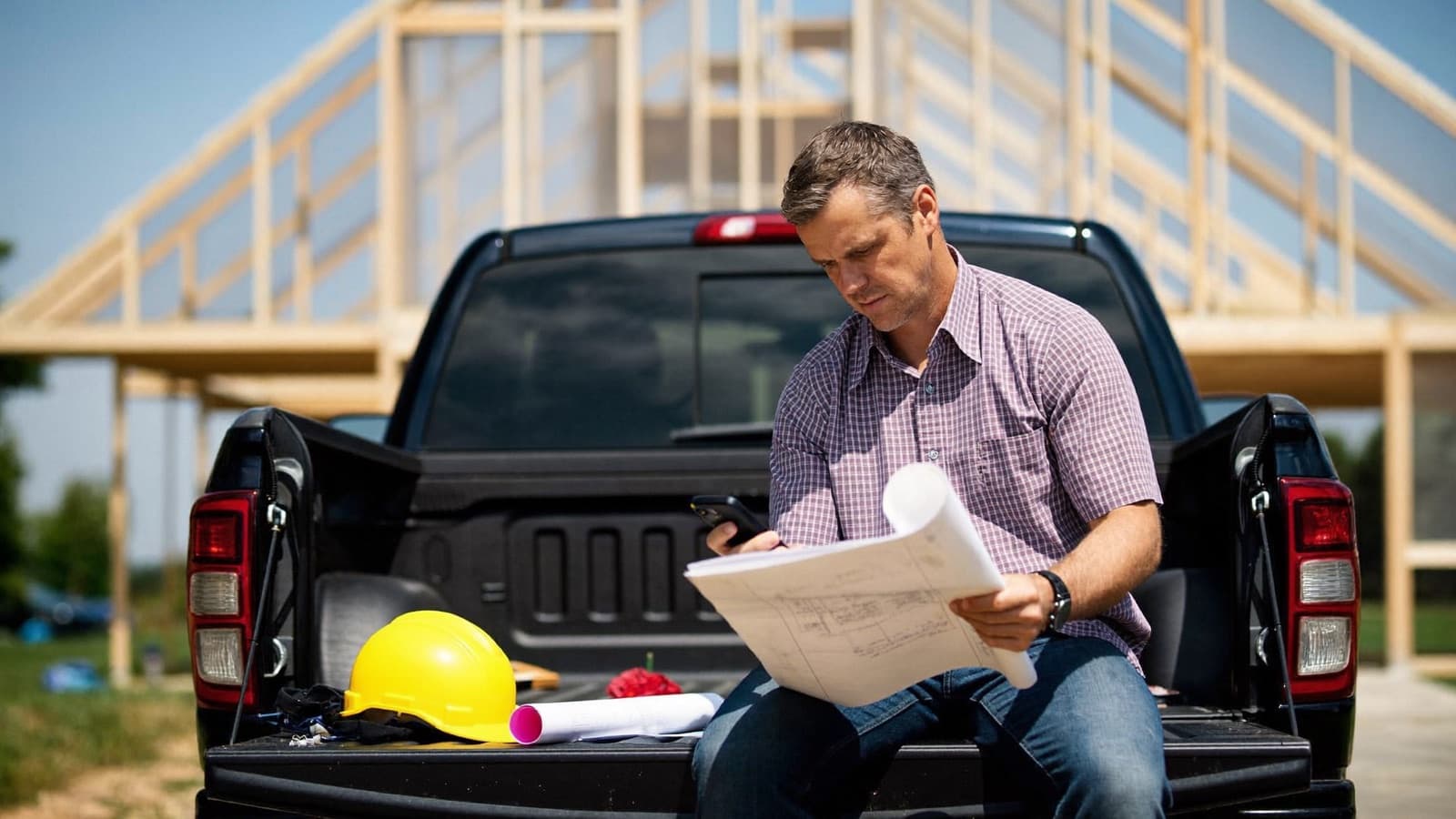 A contractor reviewing plans and his phone at his truck tailgate on a jobsite