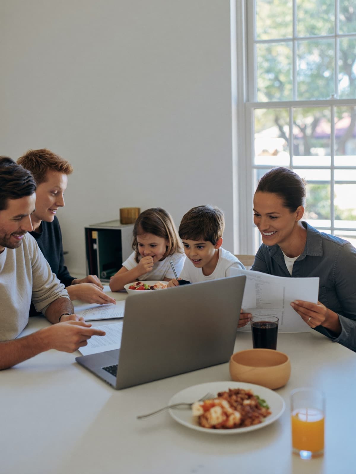 A family at their kitchen table reviewing health coverage paperwork beside a laptop