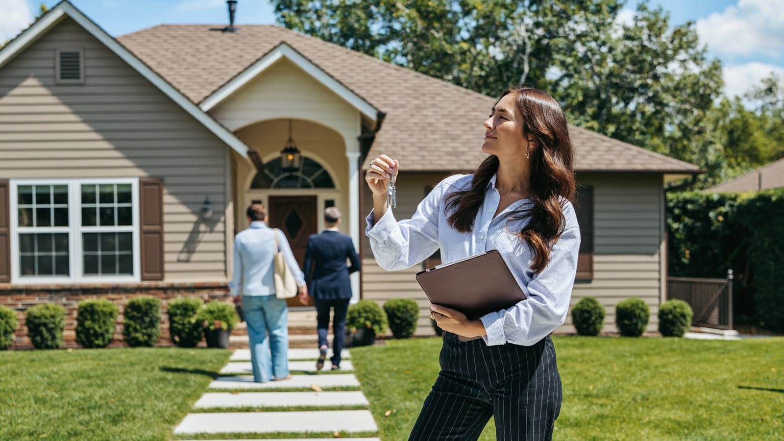 A real estate agent with a folio and keys outside a suburban listing