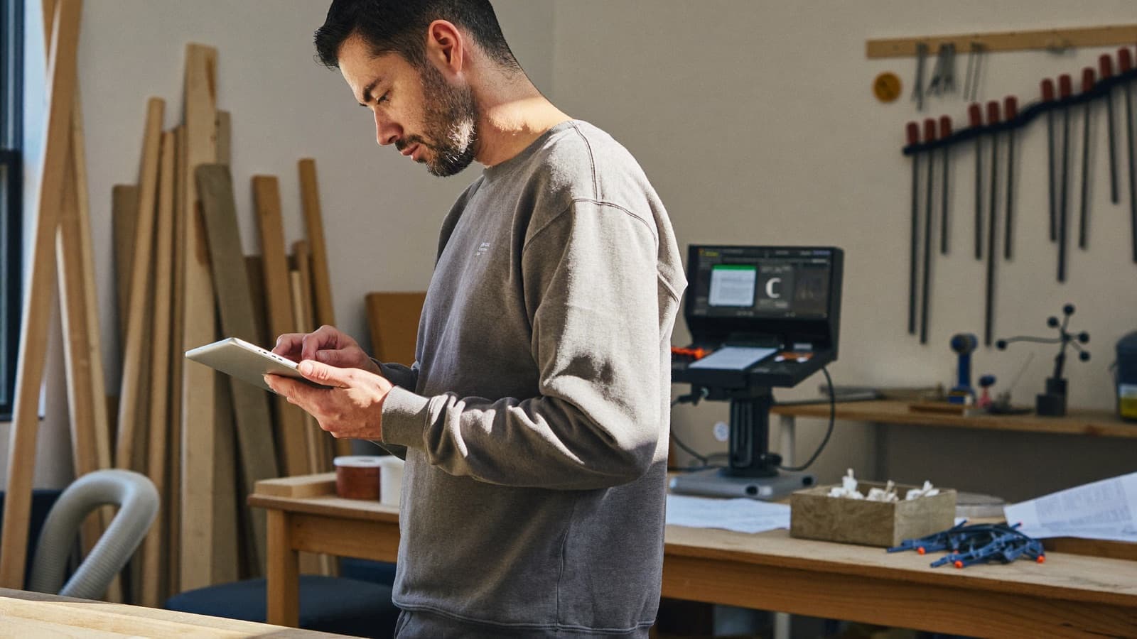 A self-employed furniture maker reviewing documents on a tablet in his workshop